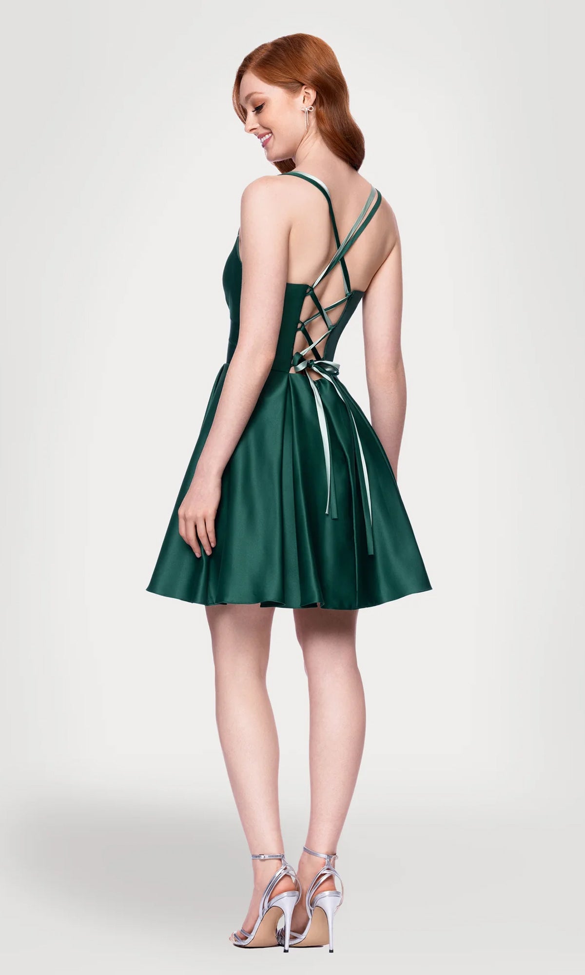 A woman models the Hunter Green Mini Hoco Dress: Blondie Nites 4927BN—a sleeveless, lace-up back A-line homecoming dress—paired with silver high heels on a neutral background.